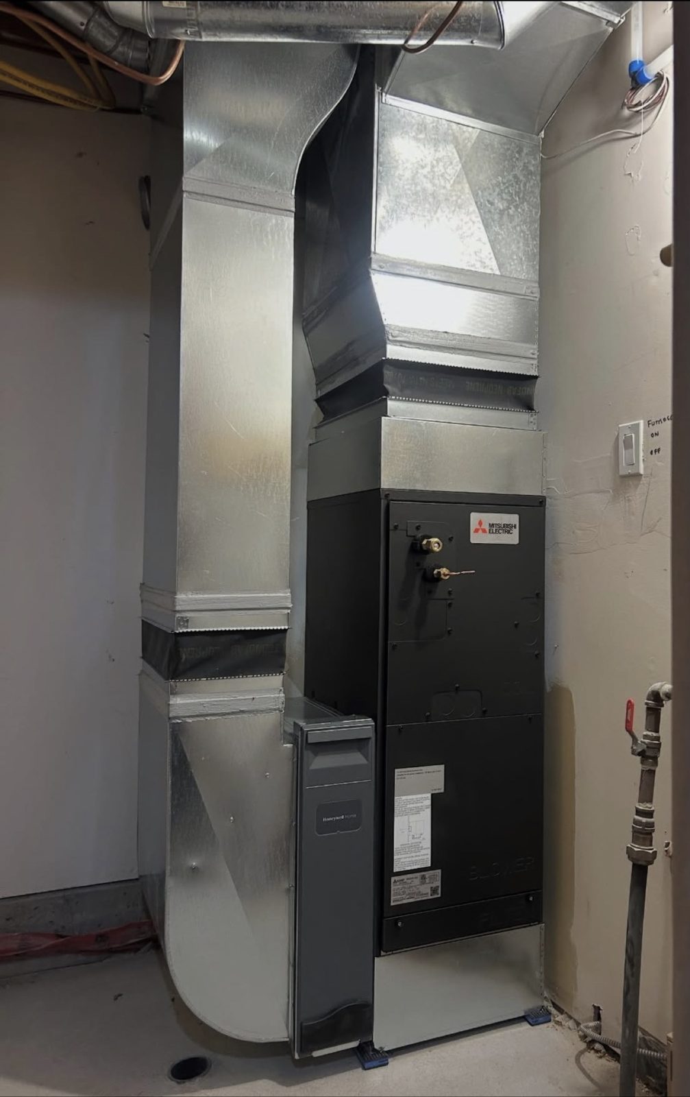 Tall view of a black Mitsubishi Electric air handler with custom sheet metal ductwork running up to the ceiling.